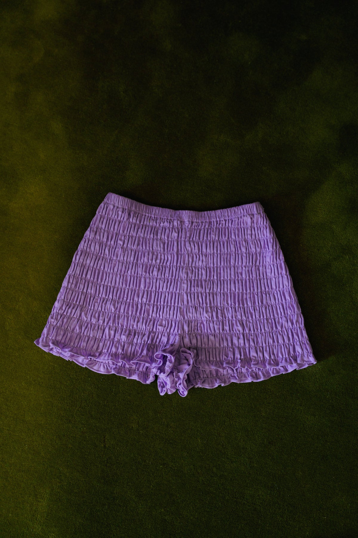 Purple smocked cotton bloomers worn with a lilac striped cardigan, showing the short silhouette and ruffled edges.