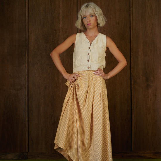 Rosemary Skirt in CandyCorn gingham styled with a cream vest and brown boots, with the hem lifted to show movement.